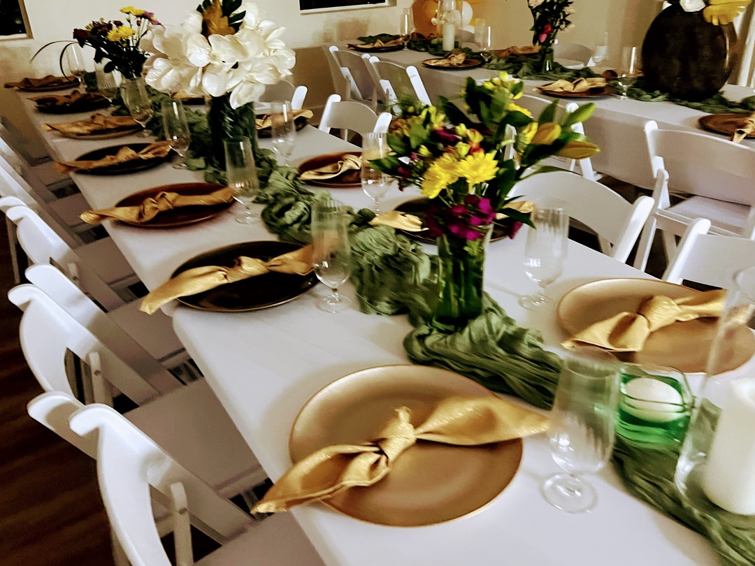 Banquet table set with gold chargers, green glassware and white florals at The Ivy House